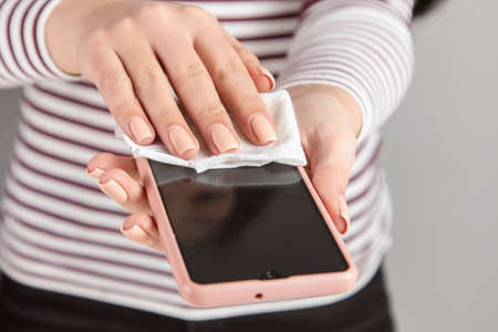 Woman cleaning mobile phone with antiseptic wipeの写真素材
