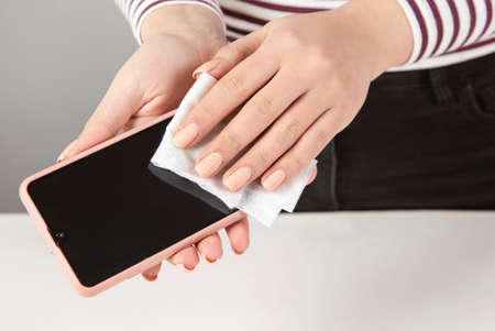 Woman cleaning mobile phone with antiseptic wipeの写真素材