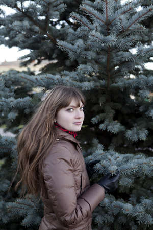 beautiful girl with dark hair, wearing a brown coat against the green pineの写真素材