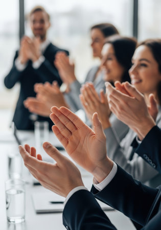 A diverse business team applauds, celebrating success in a bright office setting. The image focuses on hands clapping, conveying teamwork, achievement, and positive corporate culture.の素材