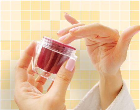 Female hands with a cosmetic cream on the yellow backgroundの写真素材