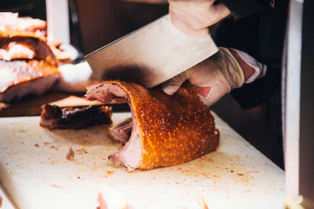 Close up view of hands chopping roast pig ribs with a large meat cleaverの写真素材
