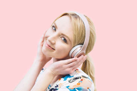 Front view of a young Caucasian girl with headphones on and listening to music on a pink backgroundの写真素材