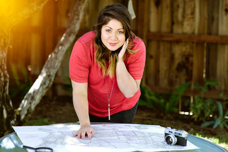 A young latina woman plans her road trip with a map and a camera in warm lighting