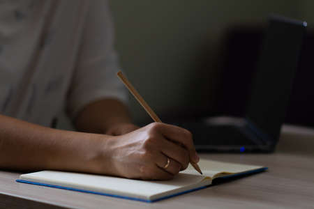Female hand with a ring writes in a notebook with a pencil. Horizontal view.の写真素材