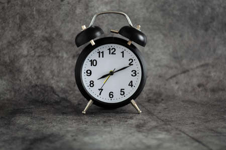 Small vintage black alarm clock on the table. black numbers, black and yellow clock hands. Clock on...