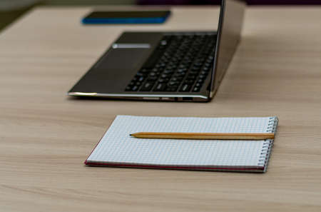 Workplace of an office worker in lockdown. Blank notepad with pencil, laptop and blue phone....
