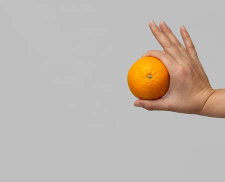 Woman holding orange in her fingers as a symbol "OK". Light gray background. Horizontal view.の写真素材