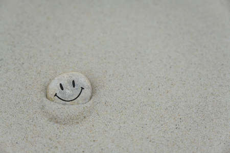 Pebble with smiley face on it lying in the sandの写真素材