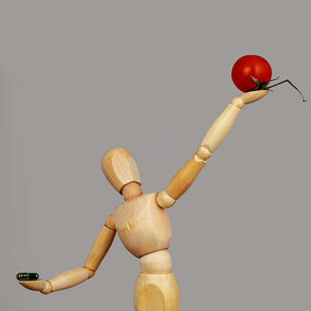 Wooden doll holding up a cherry tomato, in the other hand a vitamin tablet