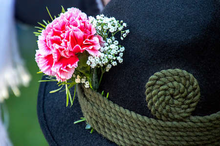 close up of a black  hat made of loden with carnation and gypsophila and a green cord