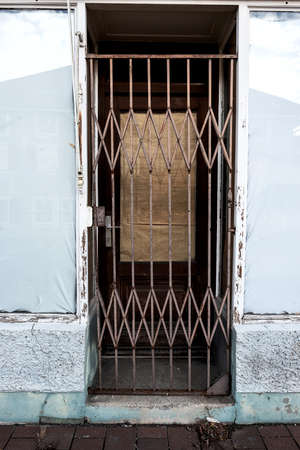 Door of an abandoned shop secured with a steel grille, the windows sealed with paper and foilの写真素材