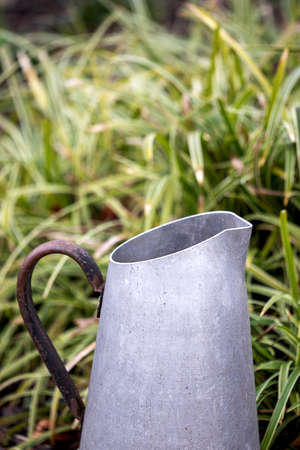 upper part of an old metal jar used for watering plants, in front of grassの写真素材