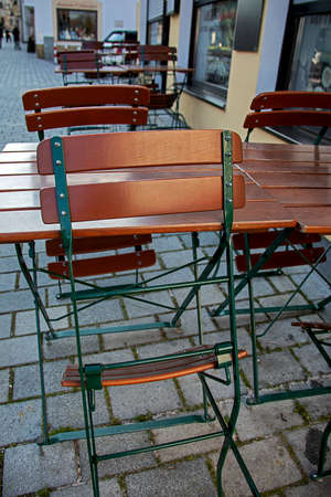 folded up beer garden chairs and empty tables in front of a street barの写真素材