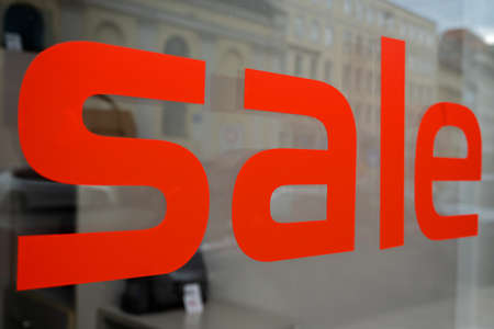 the word SALE written in red capital letters on a store window in the cityの写真素材