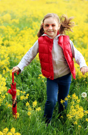 girl in a red vest and a red umbrella on a background of yellow flowers, bright colorsの写真素材