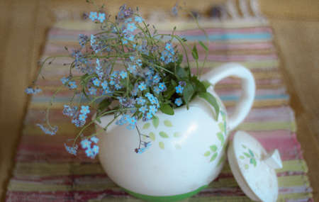 Blue flowers in a white teapot on a woven rug, selective focusの写真素材