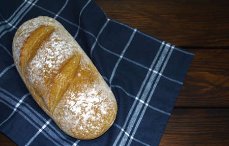 Bread, homemade bread, lies on a checkered cloth on a dark wooden table