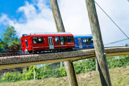 Two toy locomotives, one blue and one red, on a wooden bridge. Blue sky in the backgroundのeditorial素材