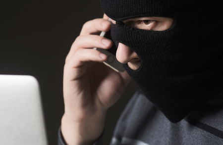 Terrorist in a mask using computer for crimeの写真素材