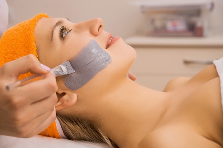 Young woman applying grey facial mask on her faceの写真素材