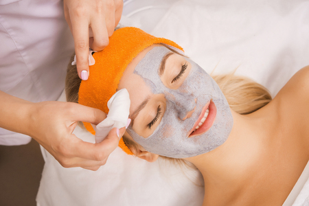 Young woman applying grey facial mask on her faceの写真素材