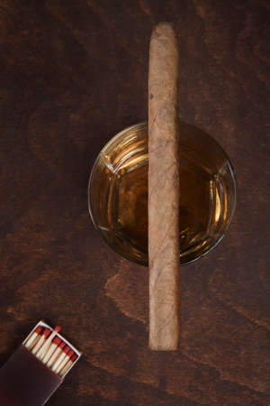 Cigar on the glass with whiskey standing on an old table 