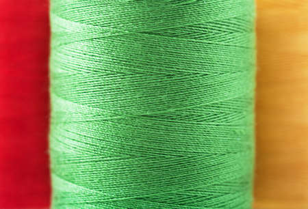 Macro view of reel of green, red and yellow thread spools 