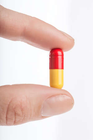Woman fingers holding a pill over white backgroundの写真素材