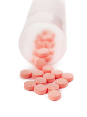 Macro view of heap of red pills spilled out of container over white backgroundの写真素材