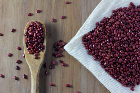 grains red bean bag on side of wooden table, wooden spoon with red beans, top view