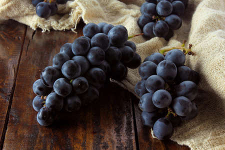 bunches of fresh grapes, with branches and leaves, on rustic fabric, on rustic wooden table