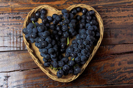 bunches of grape inside basket with heart shape on wooden table, top viewの写真素材