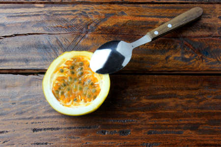 Stainless steel spoon removing yellow passion fruit pulp on wooden table. Top view
