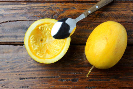 Stainless steel spoon removing yellow passion fruit pulp on wooden table. Top view
