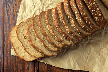 Wholegrain sliced organic bread composed of oats and flax seeds on wooden table, on paper. Healthy...