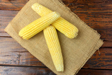 ear of raw corn, harvested from plantation, on rustic cloth, on rustic wooden table. top view