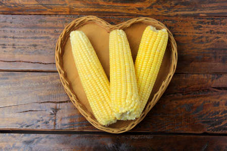 Corn cob, fresh, harvested from plantation inside basket with heart shape on rustic wooden table....