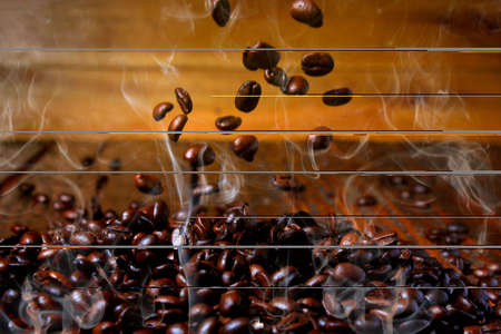 roasted coffee beans falling on stack, hot and smoky. close-up view. Rustic wood background blurredの写真素材