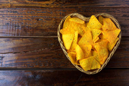 Nachos corn chips placed in basket with heart shape on wooden table, space for text