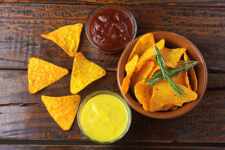 Nachos corn chips placed in ceramic bowl on wooden table next to assorted sauces
