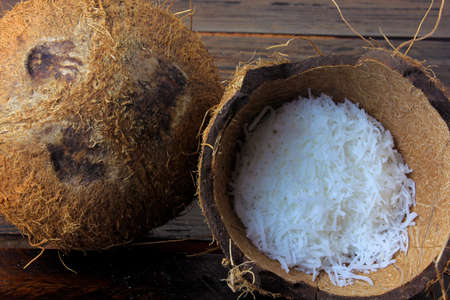 fresh coconut flakes and chips placed in bark and shell isolated on rustic wooden background