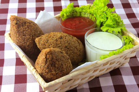 Fried kibbeh with tomato sauce in a basket, over rustic wooden table. Top view