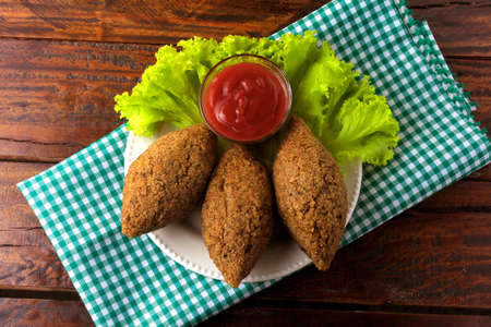 Fried kibbeh with tomato sauce on a plate, over rustic wooden table. Top view