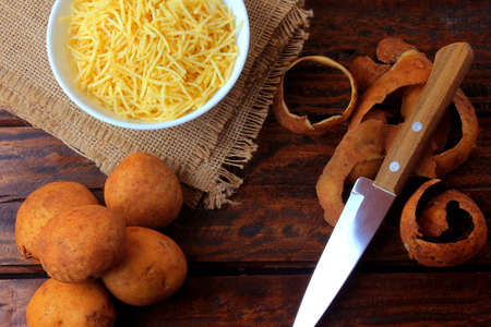 fried potato sticks in ceramic bowl on rustic wooden table with cut potatoes. Top viewの写真素材