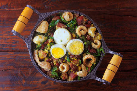 Feijao Tropeiro typical dish of Brazilian cuisine, made with beans, bacon, sausage, collard greens, eggs, on rustic wooden table. Top viewの写真素材