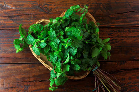Group of green organic fresh mint in basket over rustic wooden desk. Aromatic peppermint with medicinal and culinary uses. Top viewの写真素材