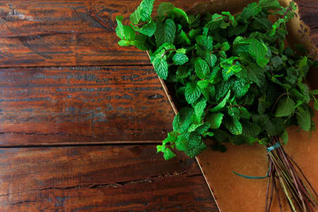 Group of green organic fresh mint in basket over rustic wooden desk. Aromatic peppermint with medicinal and culinary uses. Top viewの写真素材