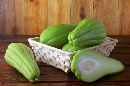 raw, fresh and organic chayote, whole and sliced in basket on rustic wooden tableの写真素材