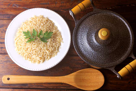 brown rice cooked in the dish next to pot and bamboo spoon in the kitchen on rustic wooden table. Top viewの写真素材